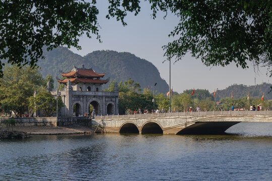 People visit the ancient stone bridge and gate at the entrance to the Hoa Lu Ancient Capital, Ninh Binh, Vietnam. Tourists explore the historic landmark.