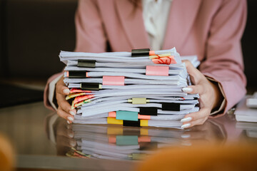 Close-up of a businesswoman reviewing a stack of organized documents with colorful tabs and clips at a desk, representing paperwork management, office organization, and administrative work.