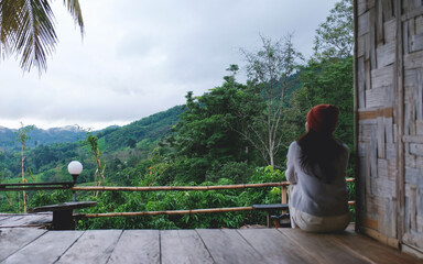 Fototapeta premium Blurred of a woman sitting on wooden balcony, looking at mountain views on cloudy morning