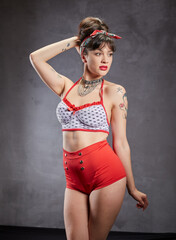 Obraz premium A woman with a fit figure and stylish clothes is posing in a studio. She is wearing red shorts and a polka-dot top.