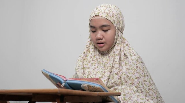 Peaceful young Asian Muslim teenage girl reading the Holy Quran in her bedroom for spiritual prayer and devotion, close up portrait