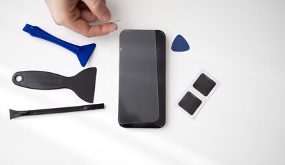 Hands cleaning smartphone display and installing tempered glass screen protector using repair...