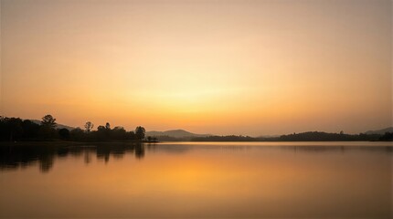 Obraz premium Golden sunset over a calm lake. Peaceful rippling water with silhouette of trees and mountain range. Natural background for meditation, relaxation, travel, vacation and tourism concept.