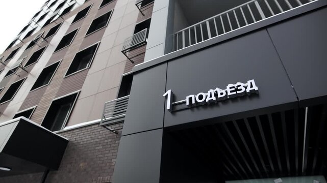 White dimensional numbers mounted on dark entrance canopy mark building section identification. Contrast creates sharp modern accent