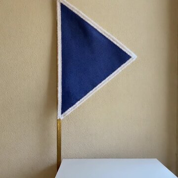 The Generic Pennant. Soccer/Football Merchandise Mockup (No Brand, No Logo). Fan Merchandise. A plain triangular felt pennant in royal blue with a white border, hanging against a textured ivory wall

