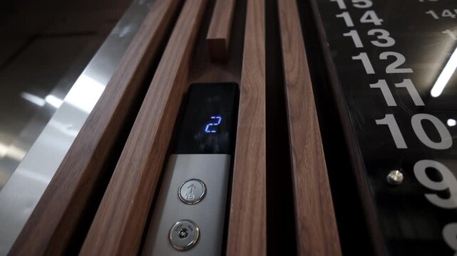 Elevator call panel displays moving cabin indicator alongside buttons for floor selection. Interface looks technological intuitive modern
