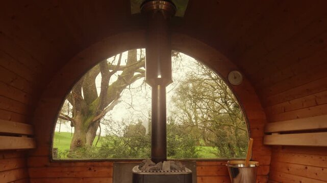 Wide view of cabin sauna revealing wood fire heating up ready for pouring water to create steam. Luxury spa treatments, self-care routines, stress reduction. Part of routine for longevity.