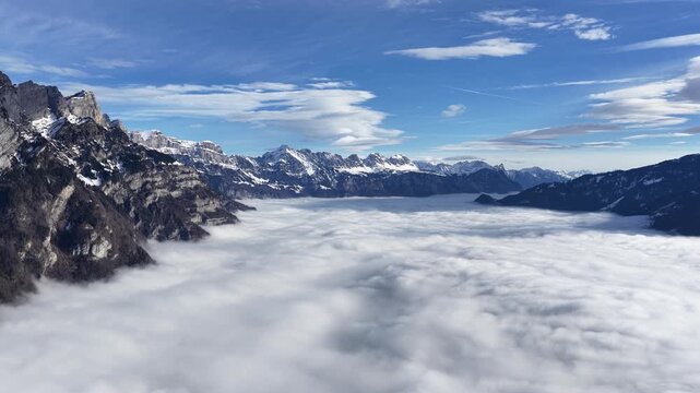 Walensee region, Switzerland aerial drone view of Swiss alps above sea of clouds near Walenstadt, Amden and Quinten, mountain landscape with winter peaks and blue sky.