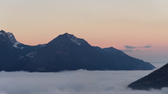 Walensee region Switzerland aerial sunrise above sea of clouds near Walenstadt and Amden, Swiss alps mountain silhouette with soft orange sky and peaceful alpine landscape.