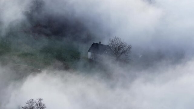 A mystical aerial shot of a lone Swiss chalet appearing through swirling mist on the slopes above Lake Walensee. A perfect symbol of mountain solitude and winter mystery.