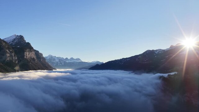 Walensee region Switzerland sunrise above thick cloud inversion between alpine mountains near Amden and Walenstadt, drone slowly pulling back fog filled valley and snowy peaks.