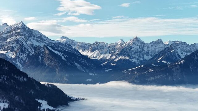 Walensee region near Amden, Walenstadt, Quinten and Mols, Switzerland, snow covered Swiss alps mountains rising above thick cloud inversion and fog valley under blue winter sky.