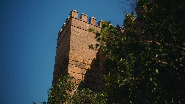 Stone fortress tower rising above greenery under blue sky