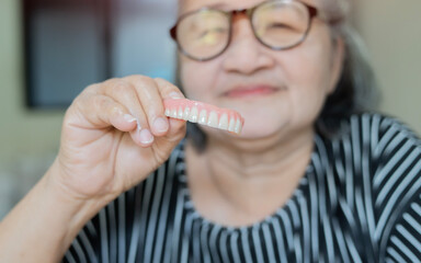 Happy senior lady holds and shows her new dental implant and jawline with a pair of teeth