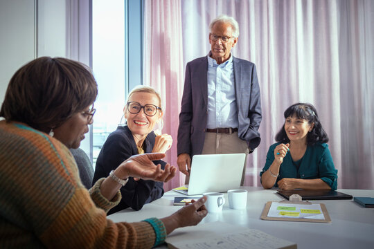 Smiling business professionals listening to colleague speaking in office meting