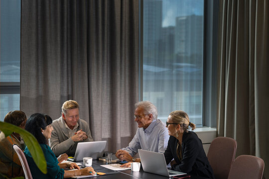 Group of smiling senior business professionals discussing while sitting around table in meeting room