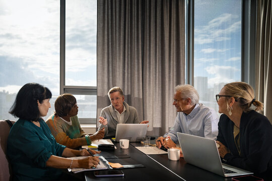 Senior businessman explaining strategies to coworkers sitting around table in meeting