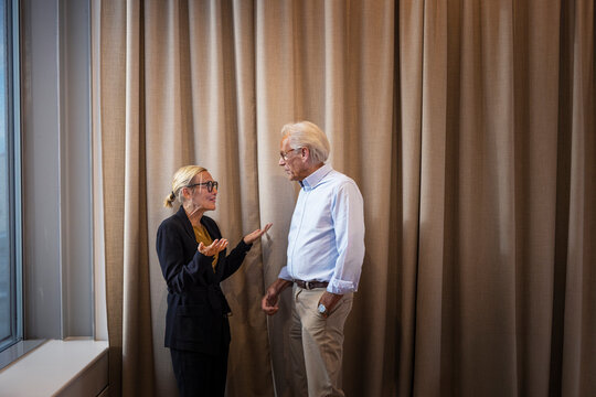 Senior businesswoman talking with male colleague standing in front of curtain at office