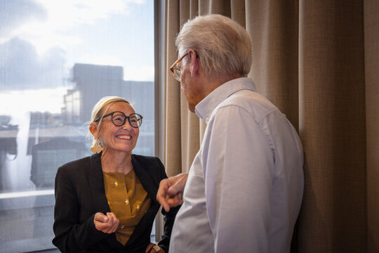 Smiling senior businesswoman talking with male colleague near window in office