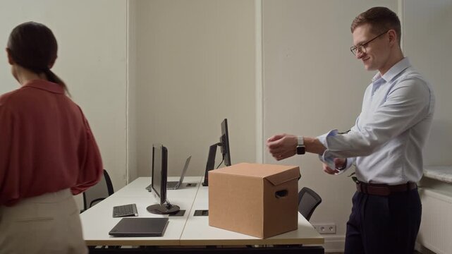 Side view of two Caucasian young colleagues arranging their workplace in modern office while unpacking stuff from cardboard boxes