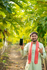 Fototapeta premium young indian farmer holding smartphone standing at papaya field