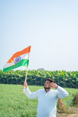 young indian farmer holding indian flag standing at green agricultural field