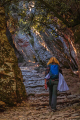 Rear view of a female hiker with a blue backpack walking along a cobbled path through a wooded and rocky gorge in the Sant Lloren&ccedil; del Munt Natural Park, Barcelona, ​​Spain.