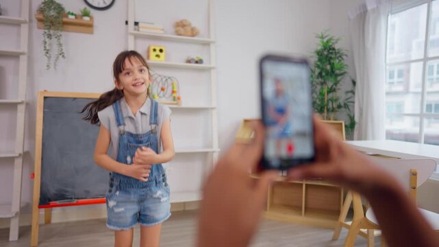African teacher use phone record young child dancing in learning space.