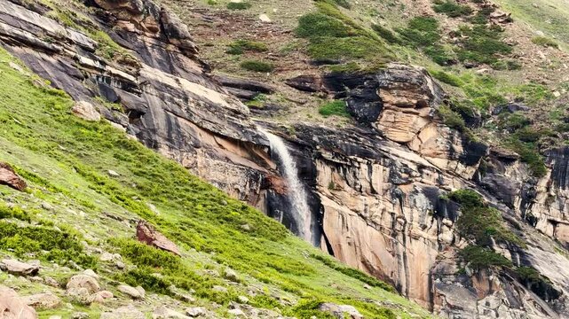 4K Landscape shot of Paralam waterfall flowing in the middle of the Himalayas as seen from Sural Bhatori in Pangi Valley, Himachal Pradesh, India. Scenic view of waterfall in the summer season.