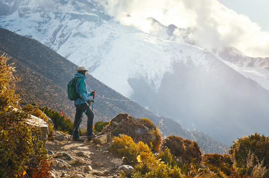 Woman hiker admires sunset on trail leading to Everest Base Camp with Himalayan Mountains surrounded by snow-capped peaks in background, Nepal.