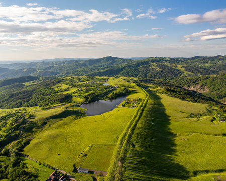 Aerial view of a serene lake mirroring the sky amidst rolling green hills, divided by a long line of trees, Vintileasca, Vrancea, Romania.
