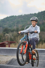 Obraz premium Older brother riding a mountain bike over rollers on an outdoor pump track while his younger sibling follows behind