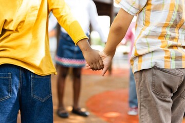 Fototapeta premium Two children holding hands, one in a yellow shirt and jeans, the other in a plaid shirt and brown pants. Children holding hands, symbolizing friendship and unity among diverse school kids.
