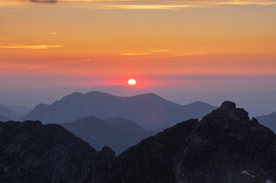 Aerial view of the sun setting behind the majestic peaks of Satan, casting an orange glow across the landscape, Vysoke Tatry, Presov Region, Slovakia.