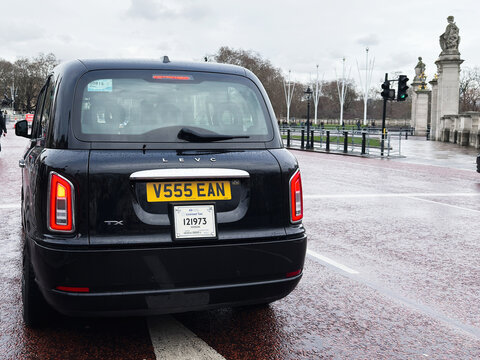 London black LEVC taxi on a wet street near historic monuments and pedestrians in motion