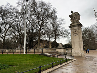 Obraz premium Statue on a stone pedestal beside a London bridge with trees and pedestrians in winter
