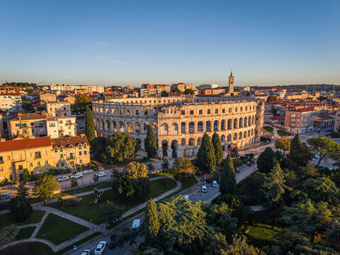 Aerial view of the ancient Roman amphitheater, a majestic stone relic amidst a city bathed in the warm glow of the setting sun, Pula, Istria County, Croatia.