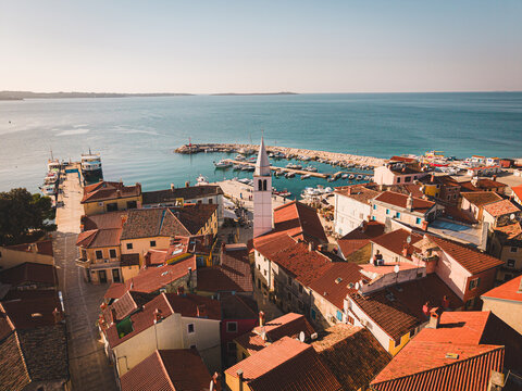 Aerial view of terracotta rooftops cascading down towards the azure sea and harbor dotted with boats, anchored under a clear sky, Fazana, Istria County, Croatia.