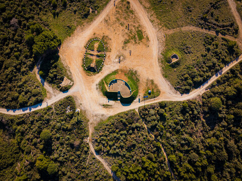 Aerial view of earthy pathways converge around ancient stone structures amidst verdant foliage, casting shadows under the Croatian sun, Pula, Istria County, Croatia.