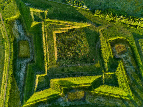 Aerial view of the Olieschans fortress, with its geometric earthworks bathed in the warm glow of sunlight, creating a striking contrast, Aardenburg, Zeeland, Netherlands.