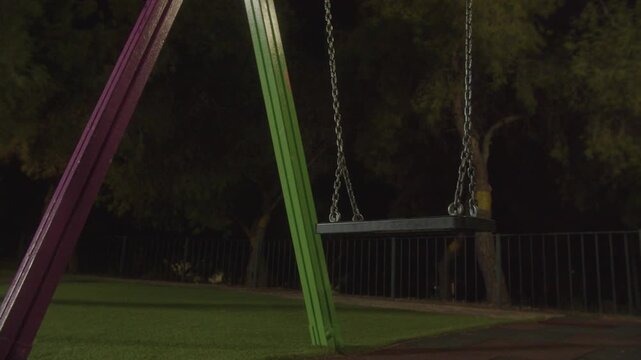 Empty swing at night in a quiet playground, evokes solitude and nostalgia