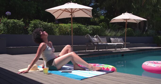 Sun is causing woman to tilt face up while sipping cold drink for sunbathing by pool