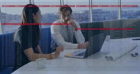 Discussing midadult colleagues in business wear gesturing to laptop at office table with plans code