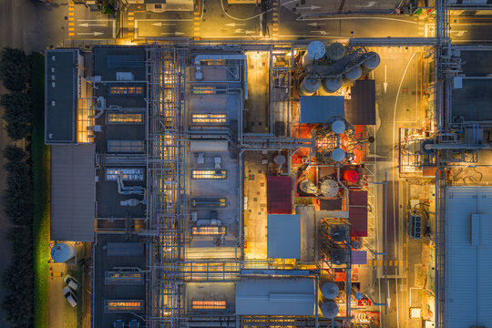 Aerial view of the industrial complex, a symphony of steel and light, where silver tanks gleam against the warm glow of sodium lamps at twilight, Settecamini, Lazio, Italy.