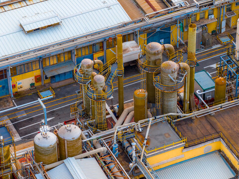 Aerial view of industrial complex with tall structures and intricate piping, reflecting a blend of aged textures and functional design, Settecamini, Lazio, Italy.