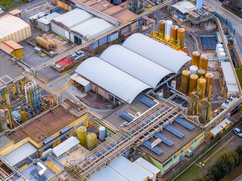 Aerial view of industrial buildings with a complex network of pipes and storage tanks, showcasing a blend of textures and tones, Settecamini, Lazio, Italy.