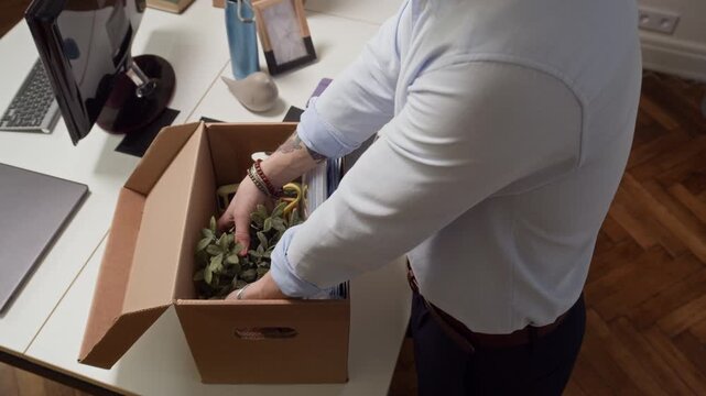 View from above of male employee unpacking stuff from cardboard box while organizing workplace in office