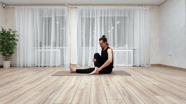 White Man Doing Seated Spinal Twist In Cozy Apartment, Gentle Rotation To Relieve Back Tension, Handsupported Turn, Core Engagement, Wooden Floor, Plant And Soft Light, Mindful Evening Flow.