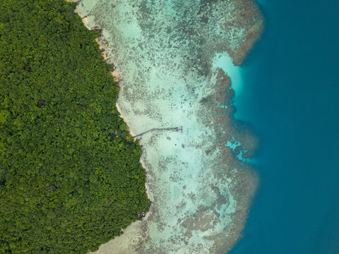 Aerial view of a lush green island meeting the turquoise ocean waters, with a dock stretching out to boats, Turtle Conservation, Karimunjawa, Central Java, Indonesia.