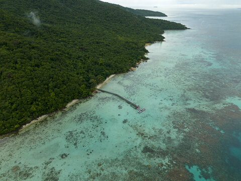 Aerial view of the lush green coastline meets the turquoise sea, revealing a wooden pier stretching out into the water at Turtle Conservation, Karimunjawa, Central Java, Indonesia.